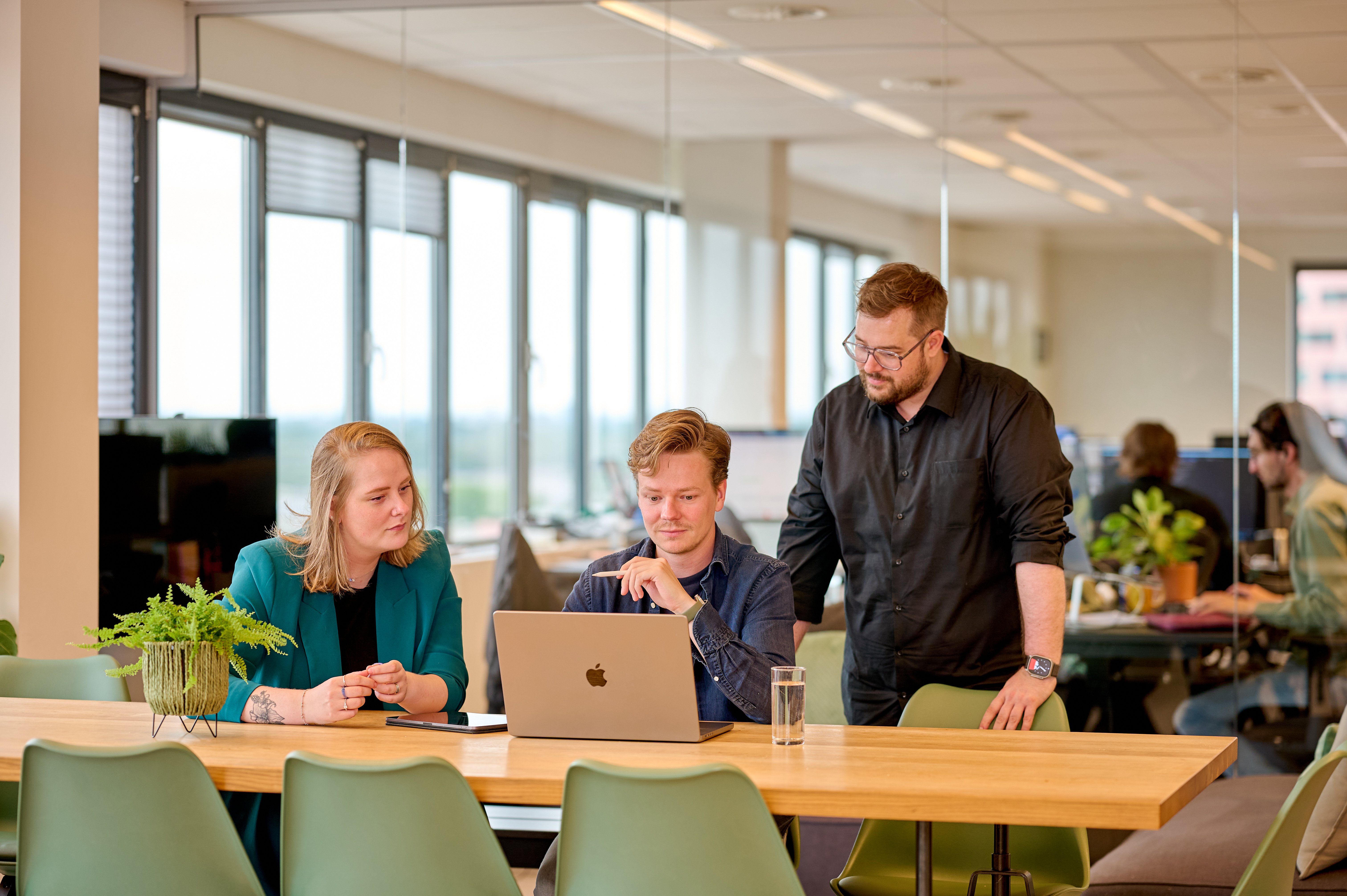 Vrouw en twee mannen op kantoor in overleg kijkend naar laptop aan een tafel
